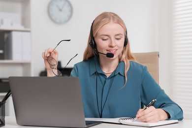 Interpreter in headset taking notes while working with laptop at table indoors