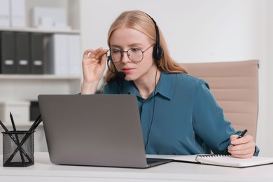 Interpreter in headset taking notes while working with laptop at table indoors