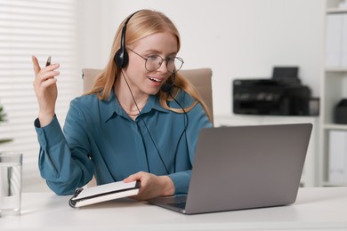 Interpreter in headset having video chat via laptop at table indoors