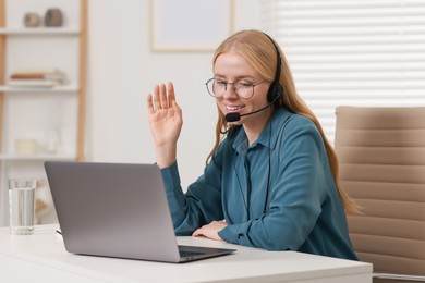 Photo of Interpreter in headset having video chat via laptop at table indoors