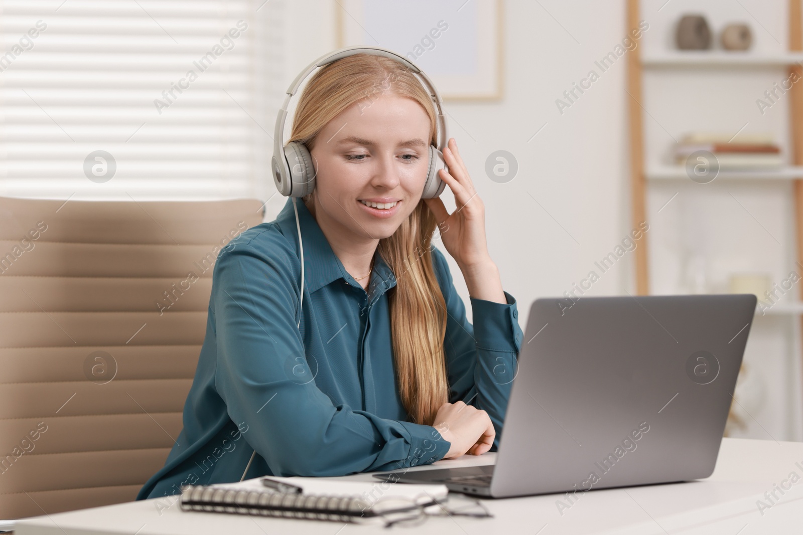 Photo of Interpreter in headphones working with laptop at table indoors