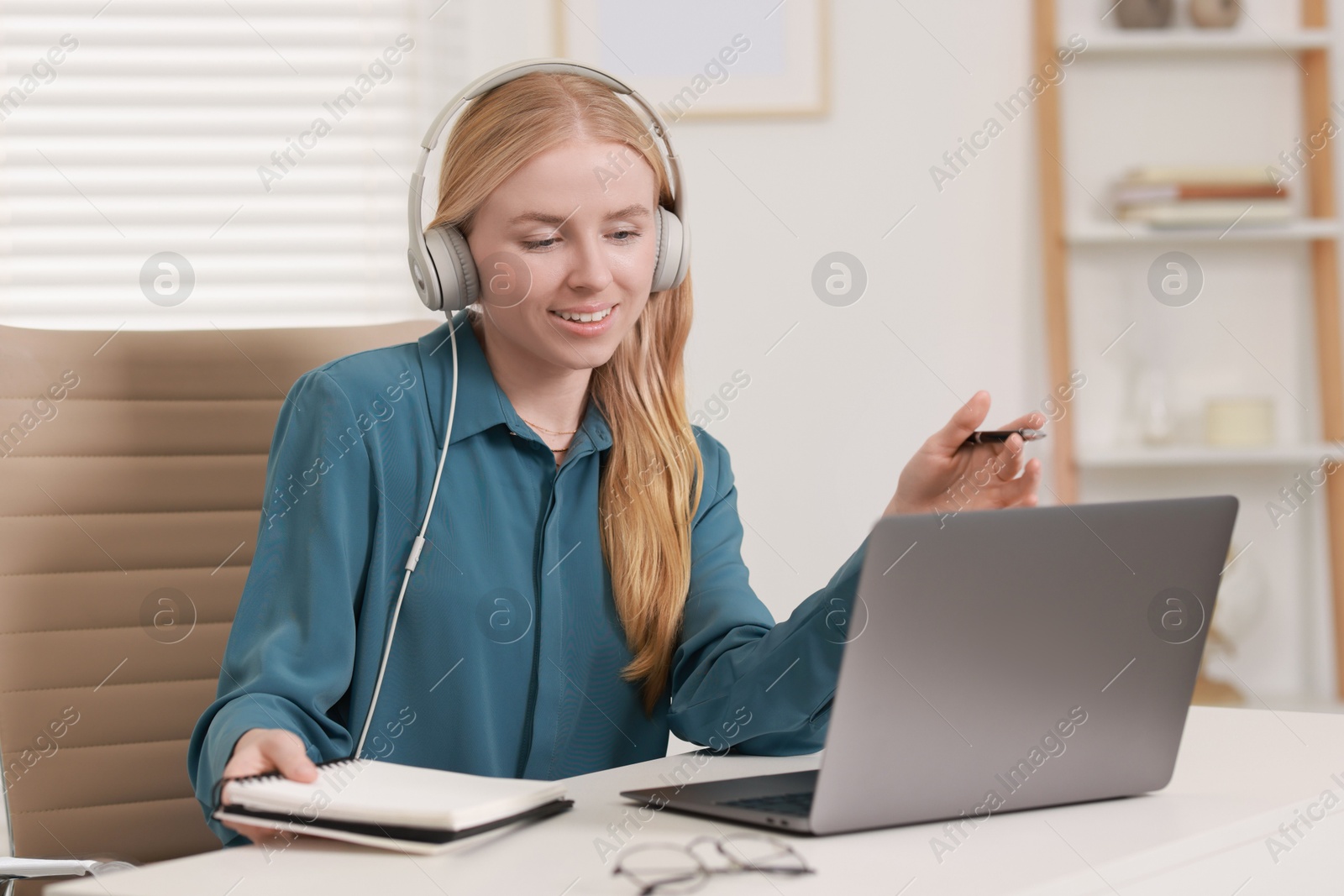 Photo of Interpreter in headphones having video chat via laptop at table indoors