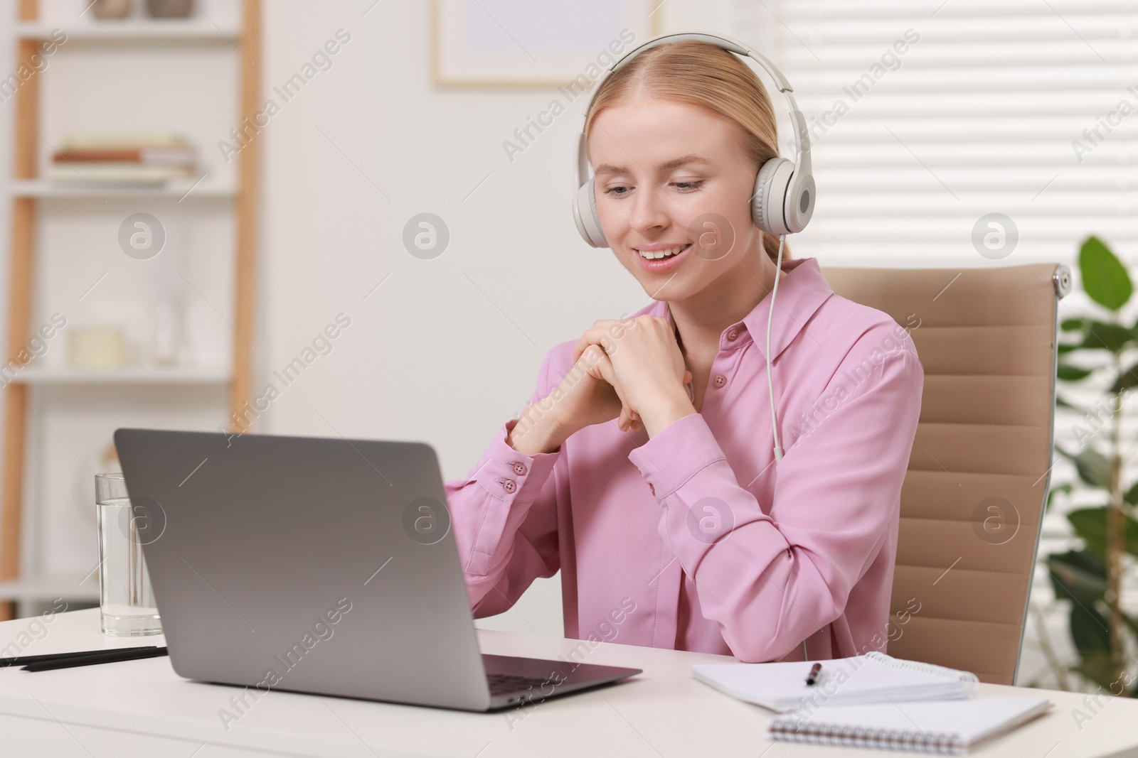 Photo of Interpreter in headphones working with laptop at table indoors