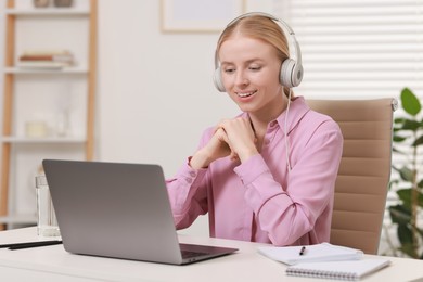 Interpreter in headphones working with laptop at table indoors