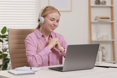 Interpreter in headphones working with laptop at table indoors