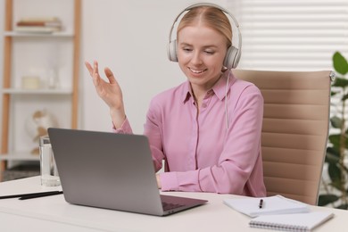 Interpreter in headphones having video chat via laptop at table indoors