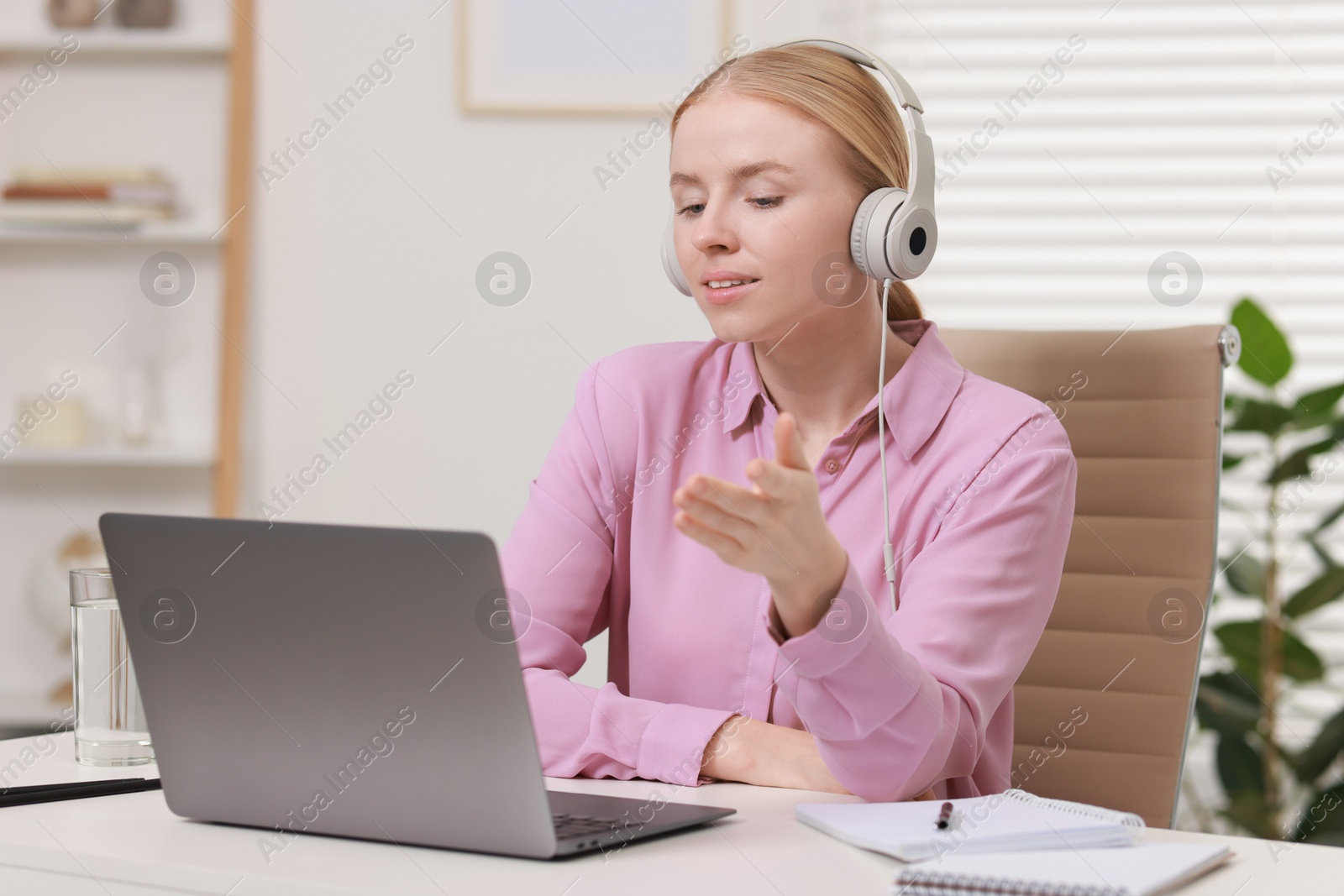 Photo of Interpreter in headphones having video chat via laptop at table indoors