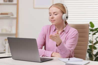 Interpreter in headphones having video chat via laptop at table indoors