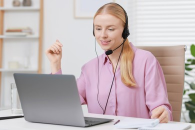 Photo of Interpreter in headset working with laptop at table indoors