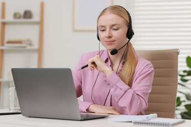 Photo of Interpreter in headset having video chat via laptop at table indoors