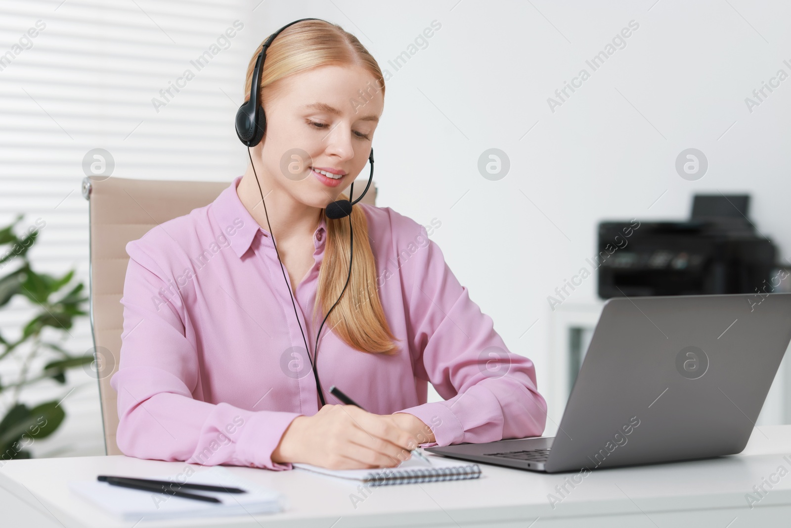 Photo of Interpreter in headset taking notes while having video chat via laptop at table indoors