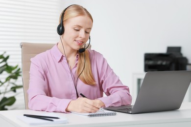 Interpreter in headset taking notes while having video chat via laptop at table indoors