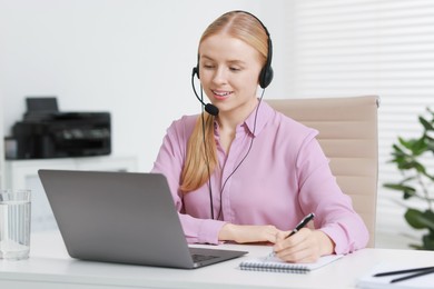 Interpreter in headset taking notes while having video chat via laptop at table indoors