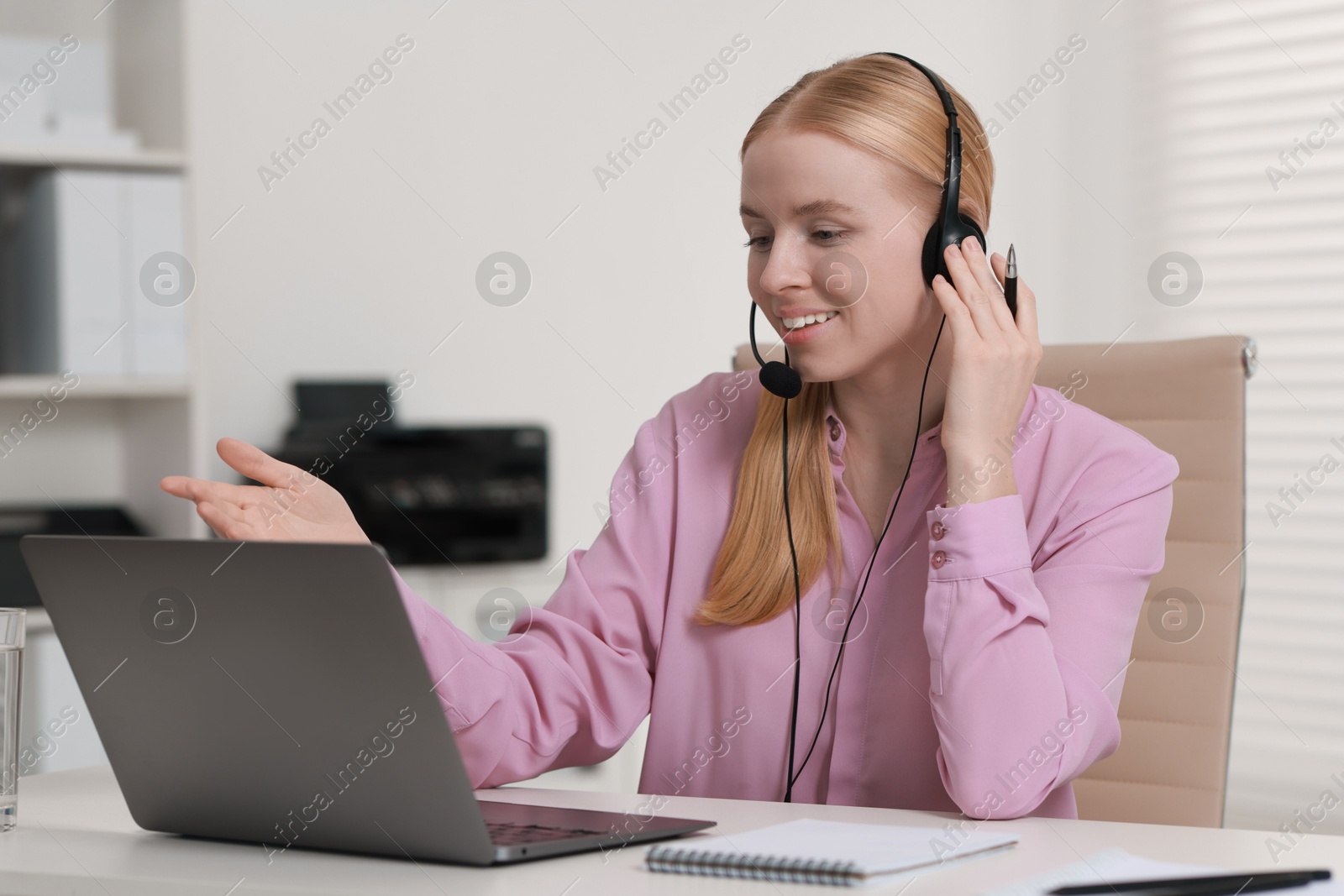 Photo of Interpreter in headset having video chat via laptop at table indoors