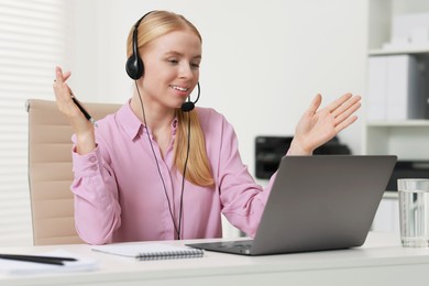 Interpreter in headset having video chat via laptop at table indoors