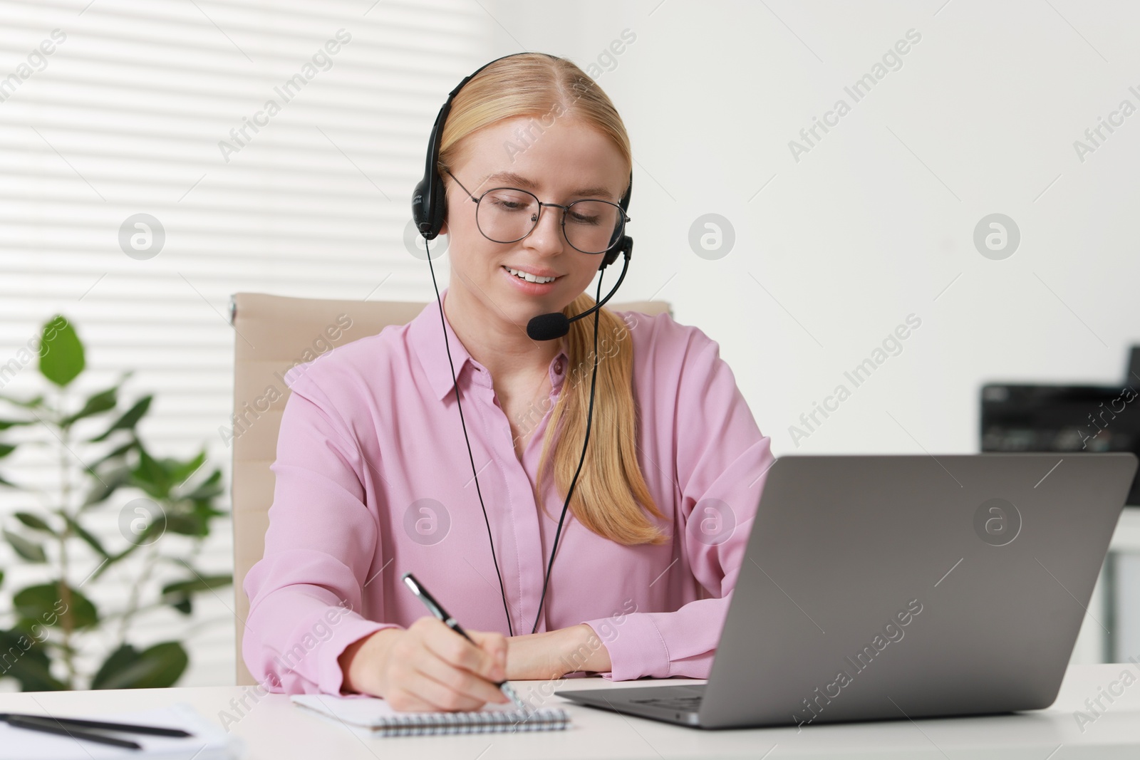 Photo of Interpreter in headset taking notes while working with laptop at table indoors