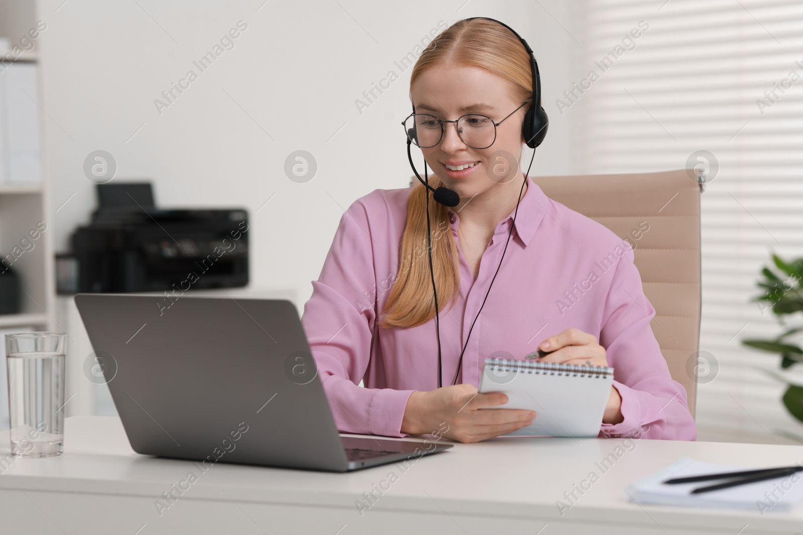 Photo of Interpreter in headset taking notes while working with laptop at table indoors