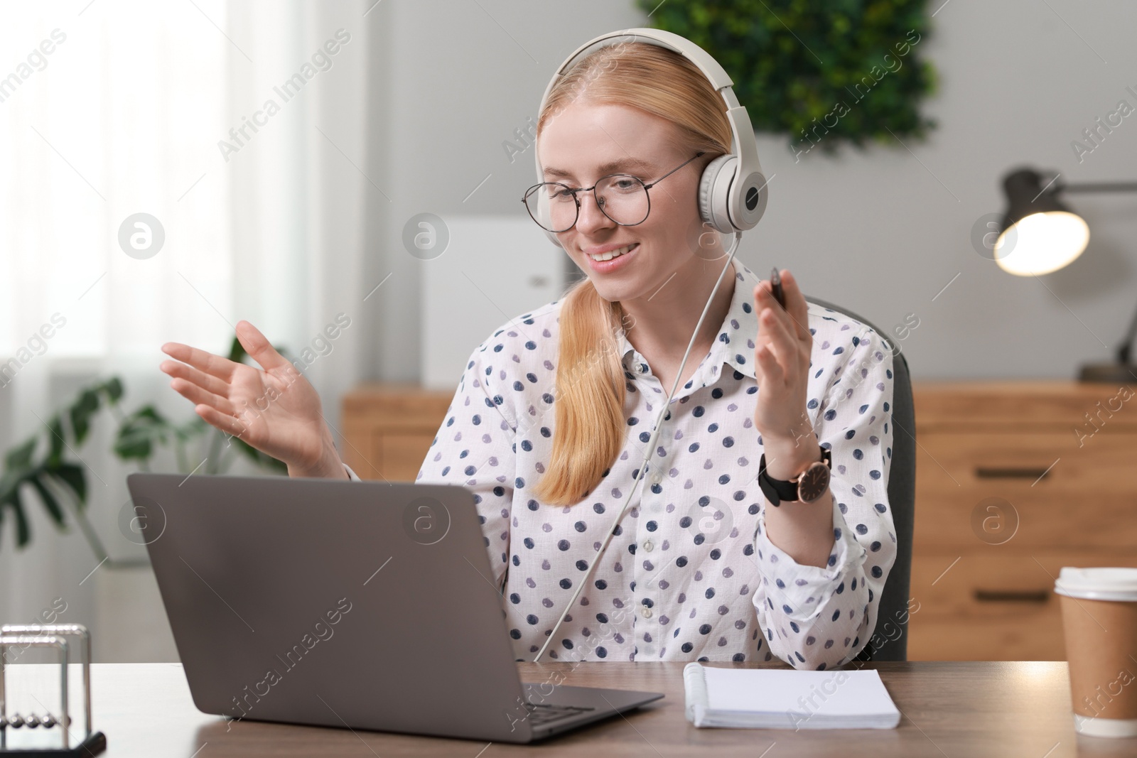 Photo of Interpreter in headphones having video chat via laptop at table indoors