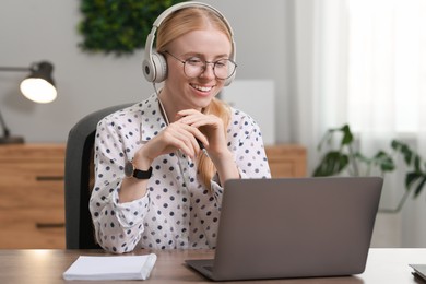 Interpreter in headphones working with laptop at table indoors