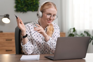 Photo of Interpreter in headphones having video chat via laptop at table indoors