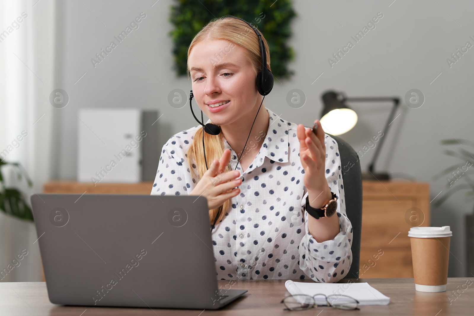 Photo of Interpreter in headset having video chat via laptop at table indoors