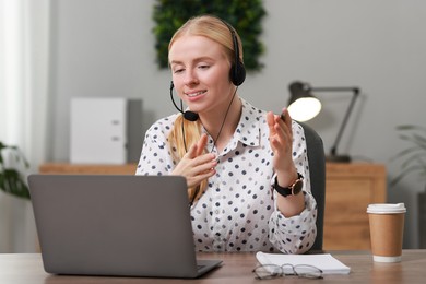 Interpreter in headset having video chat via laptop at table indoors