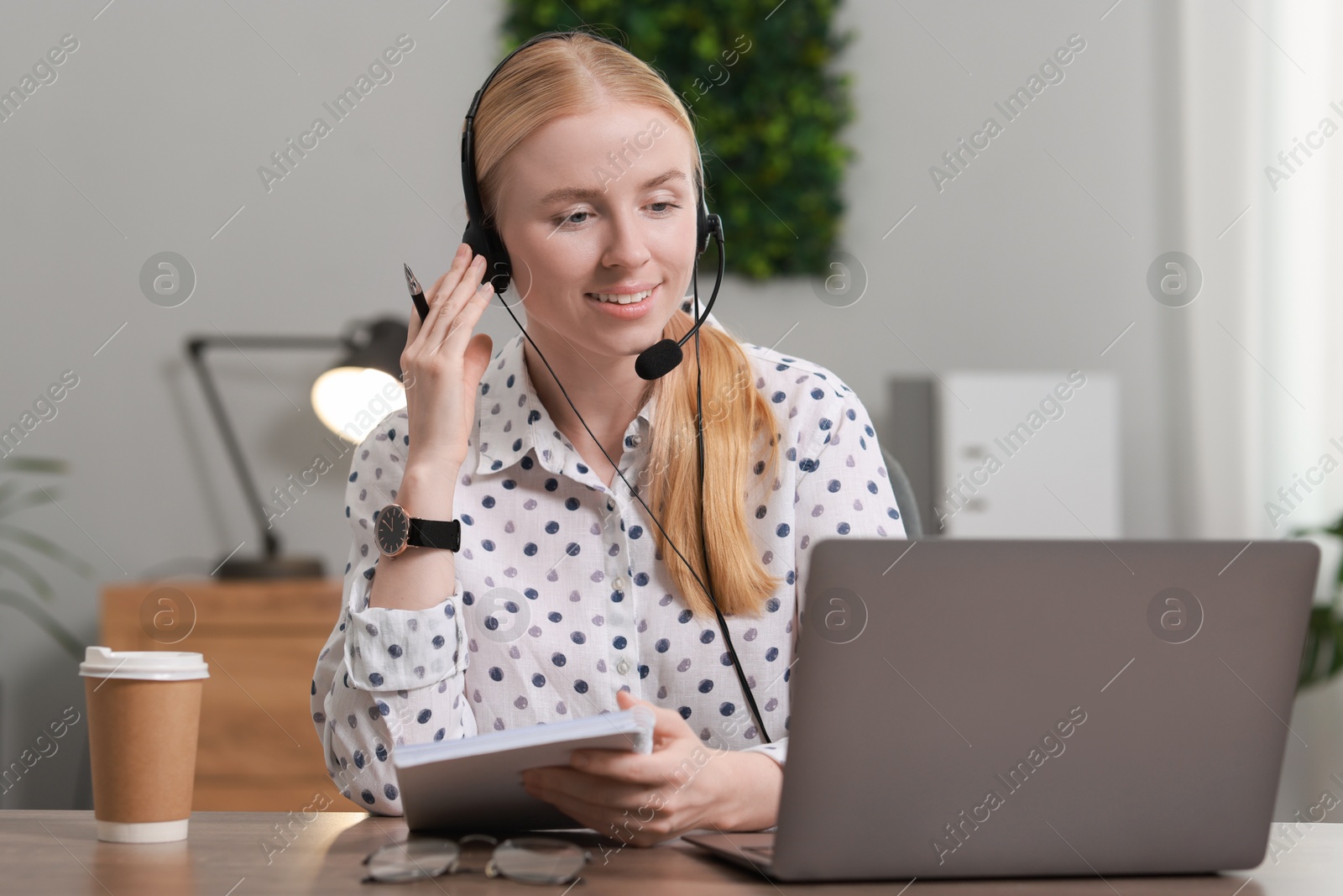 Photo of Interpreter in headset working with laptop at table indoors