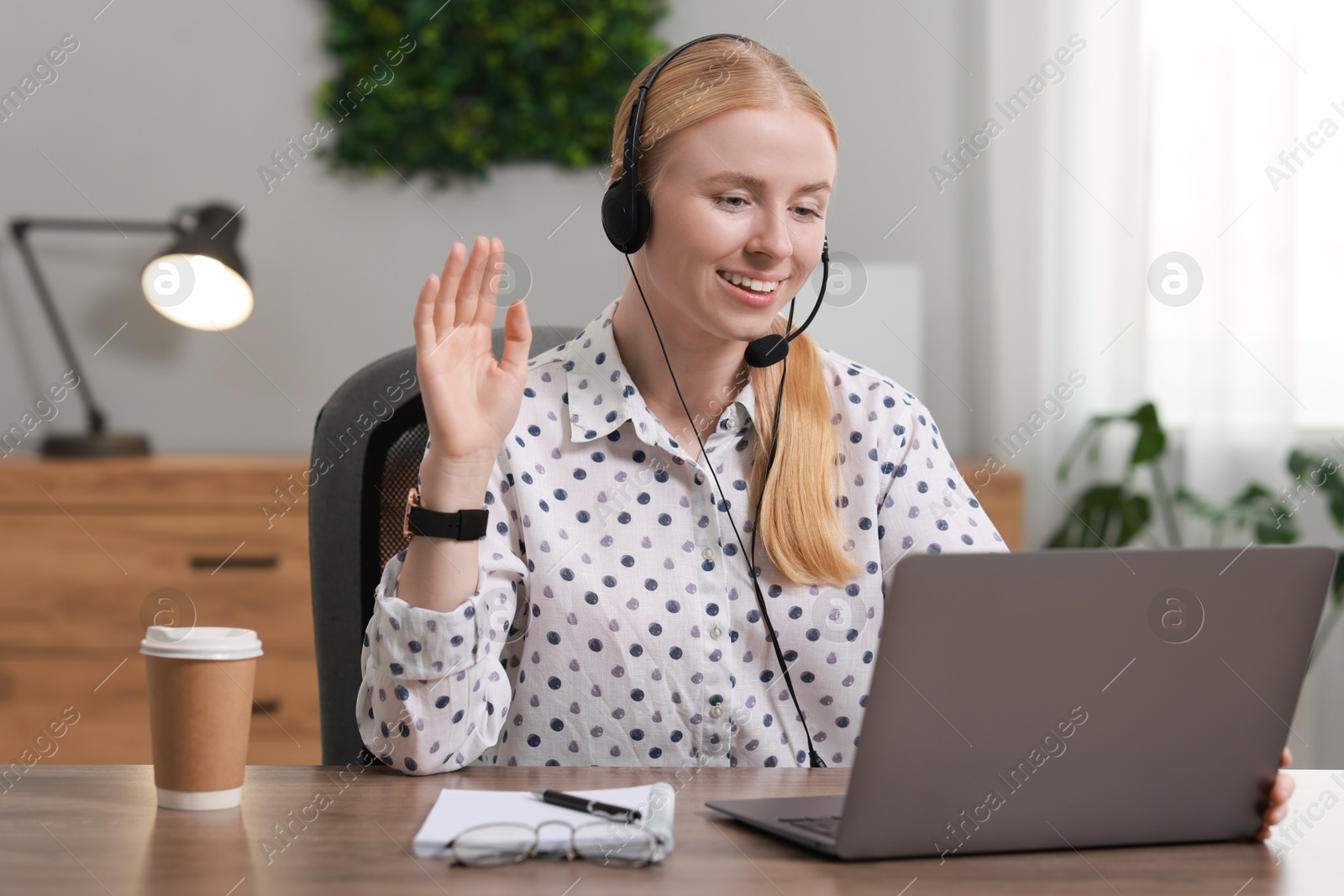 Photo of Interpreter in headset having video chat via laptop at table indoors