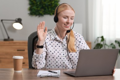 Interpreter in headset having video chat via laptop at table indoors