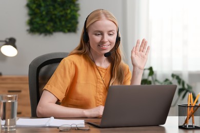 Interpreter in headset having video chat via laptop at table indoors