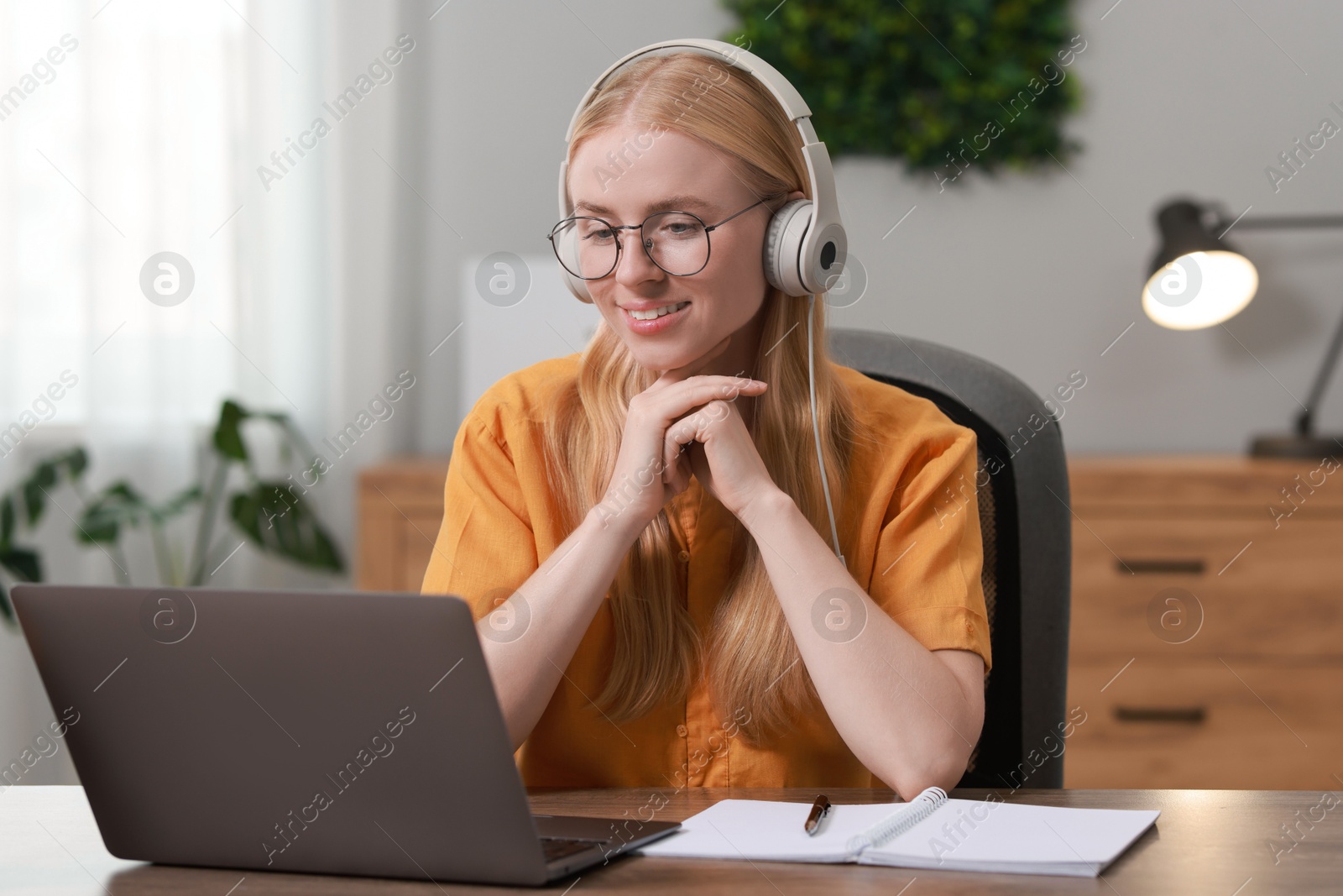 Photo of Interpreter in headphones working with laptop at table indoors