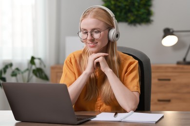 Interpreter in headphones working with laptop at table indoors