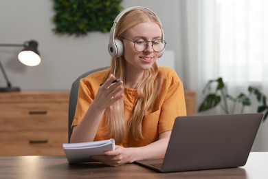 Photo of Interpreter in headphones having video chat via laptop at table indoors