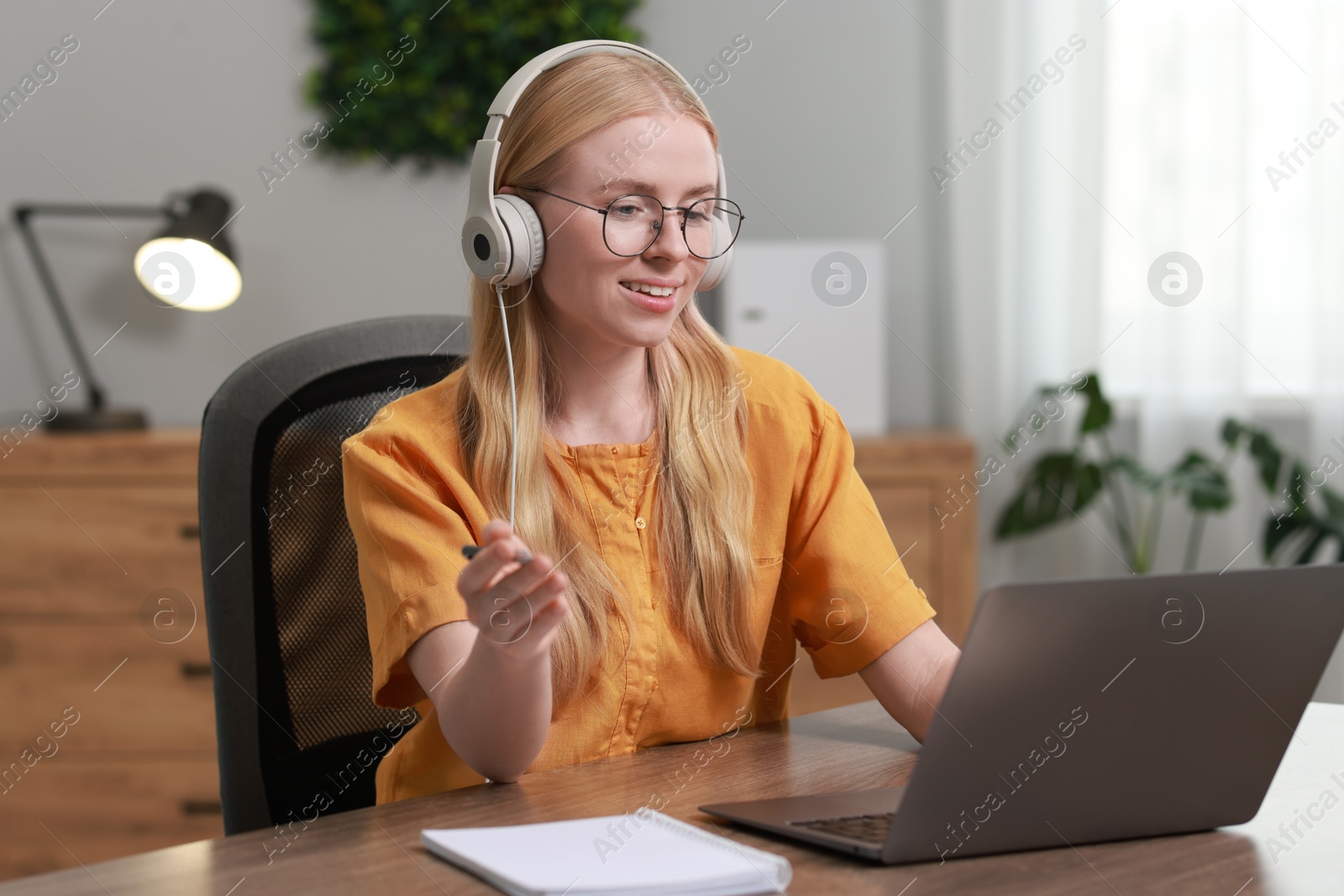 Photo of Interpreter in headphones having video chat via laptop at table indoors