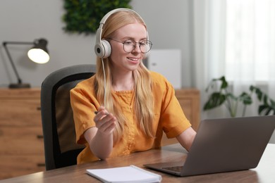 Interpreter in headphones having video chat via laptop at table indoors