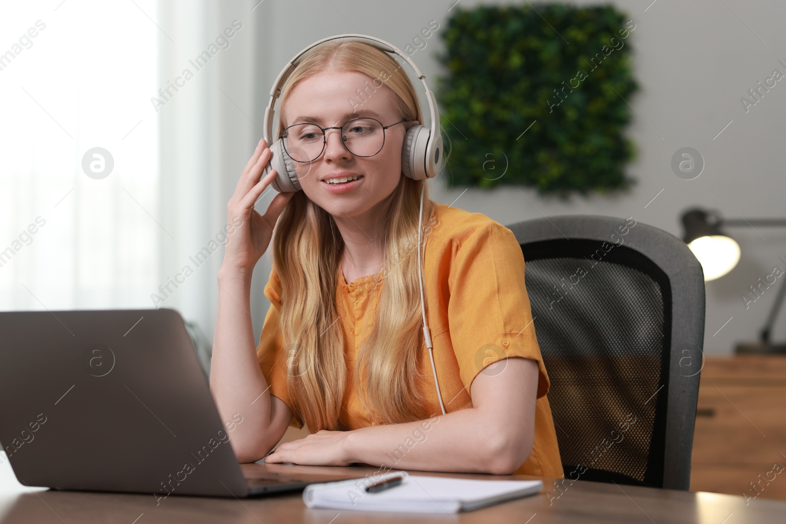 Photo of Interpreter in headphones working with laptop at table indoors