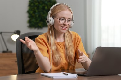 Interpreter in headphones having video chat via laptop at table indoors