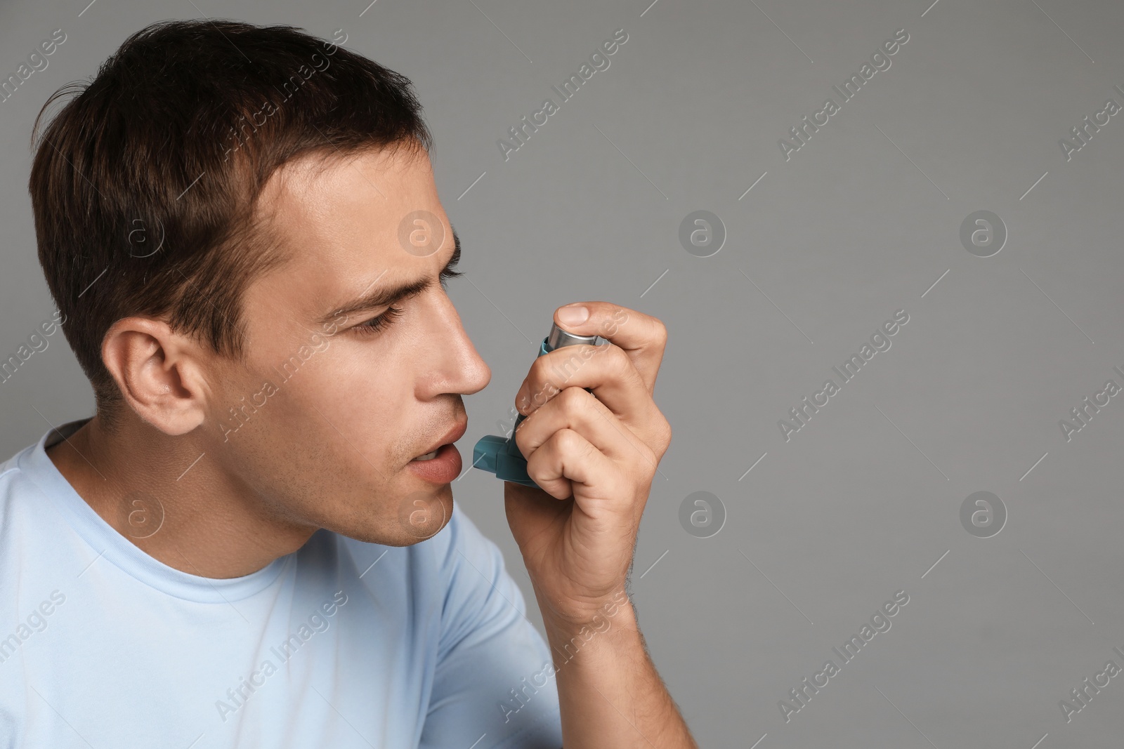 Photo of Man using asthma inhaler on grey background, space for text