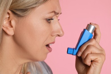 Woman using asthma inhaler on pink background, closeup