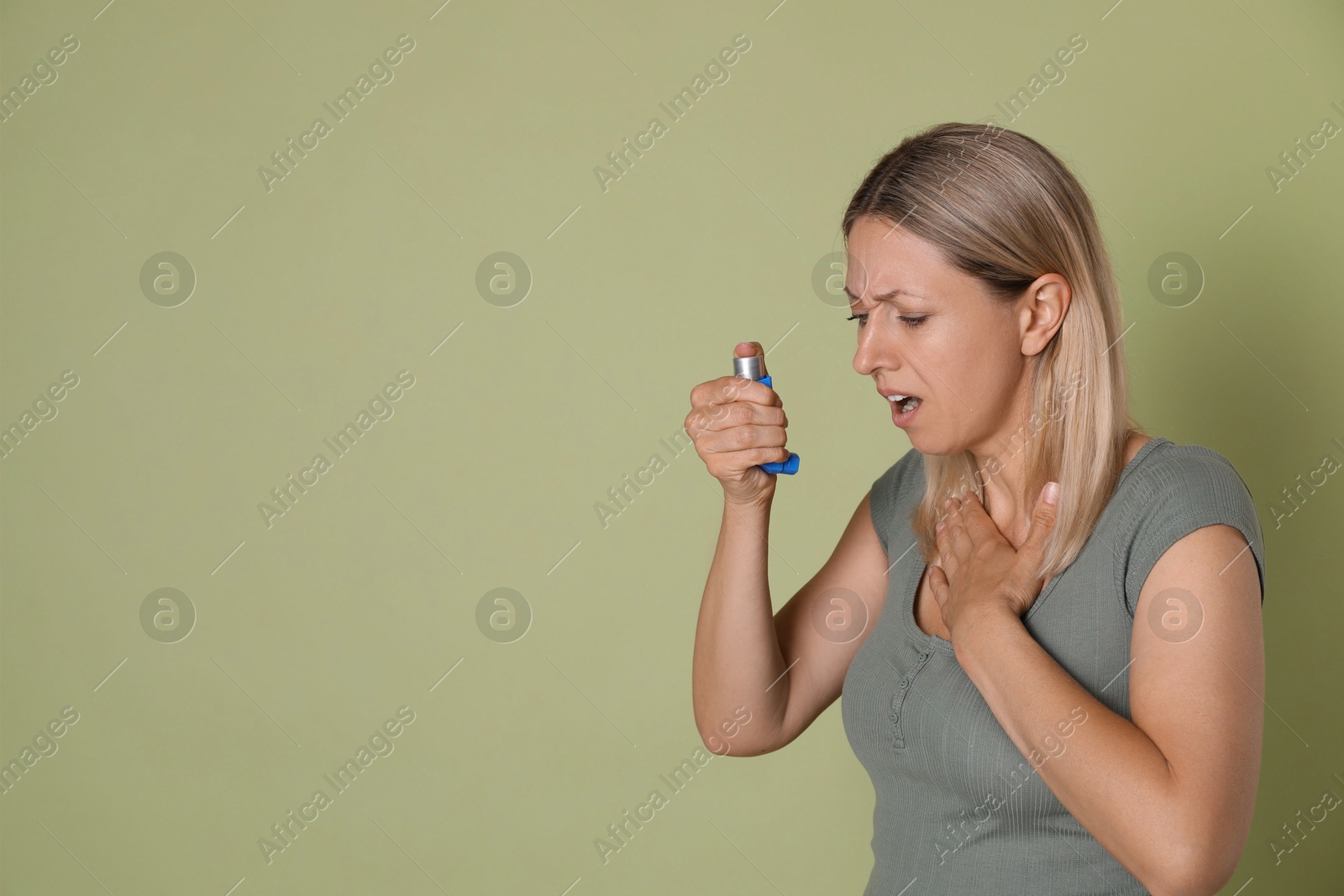 Photo of Woman using asthma inhaler on olive background, space for text