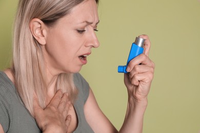 Photo of Woman using asthma inhaler on olive background