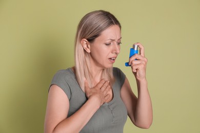 Woman using asthma inhaler on olive background