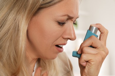 Woman using asthma inhaler indoors, closeup view