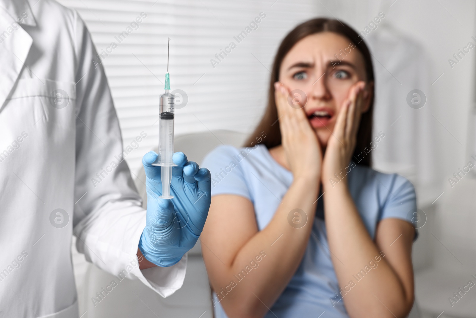 Photo of Dental phobia. Dentist with syringe near scared woman in clinic, selective focus