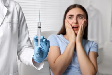 Photo of Dental phobia. Dentist with syringe near scared woman in clinic, selective focus