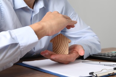 Photo of Real estate insurance. Man with wooden house figure at table, closeup