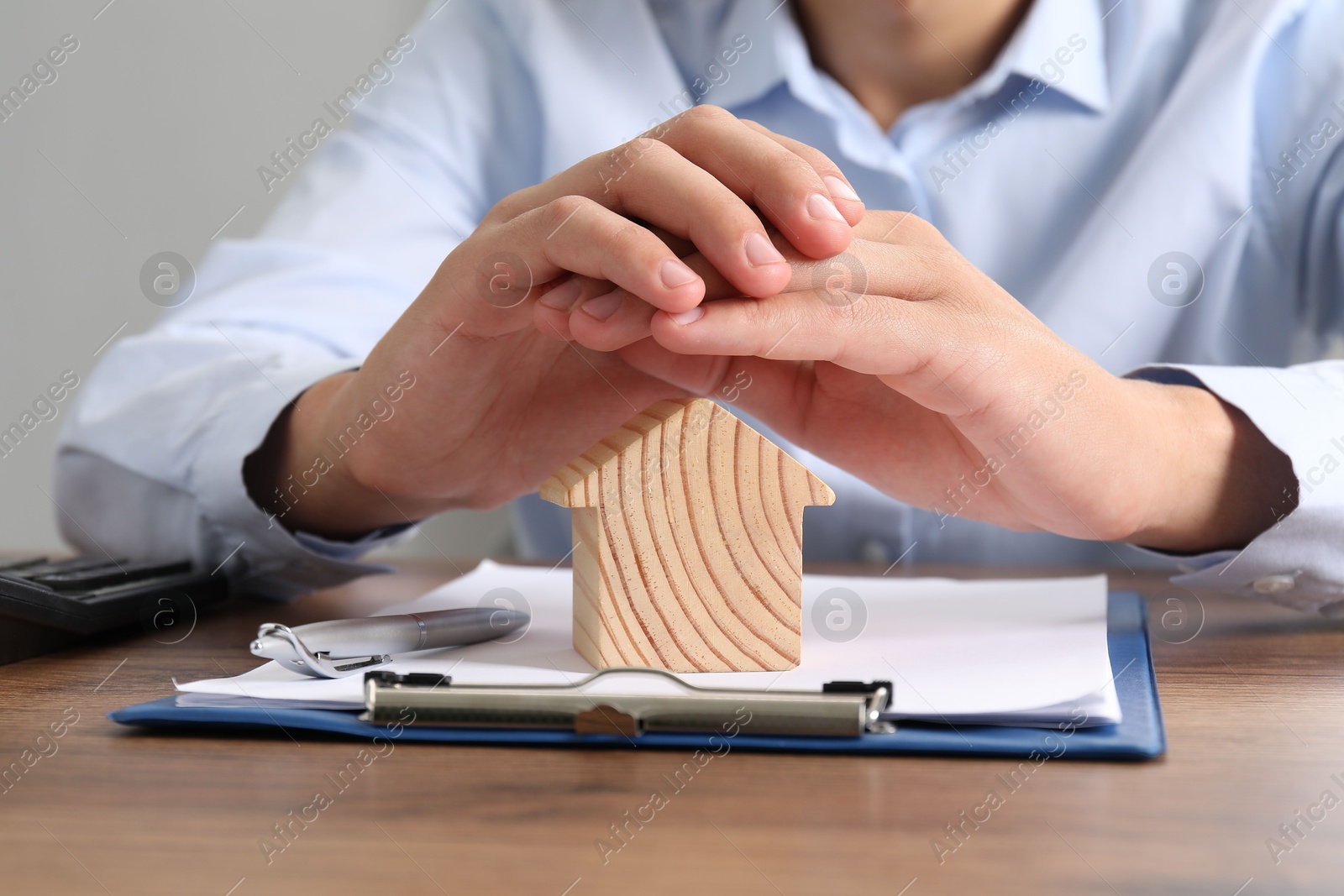 Photo of Real estate insurance. Man with wooden house figure at table, closeup