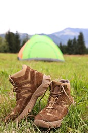 Photo of Trekking shoes and camping tent on green grass outdoors