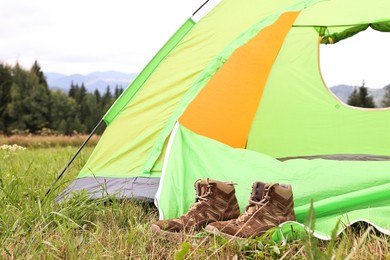 Photo of Trekking shoes and camping tent on green grass outdoors