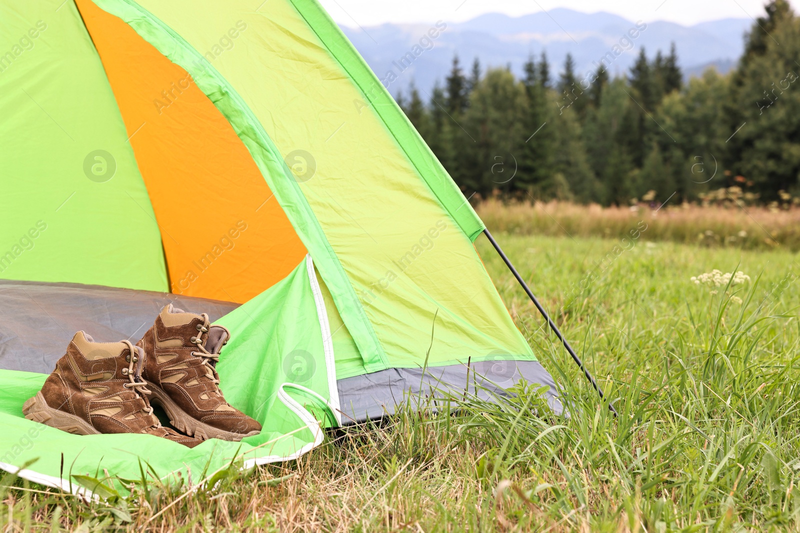 Photo of Trekking shoes and camping tent on green grass outdoors, space for text